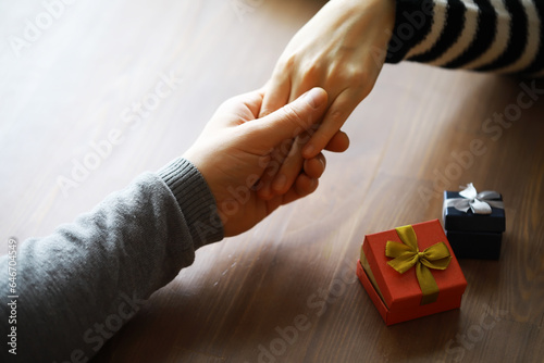 Top view of male and female hands holding gift box with ribbon on wooden background. Present for birthday, valentine day, Christmas, New Year. Congratulations background copy space.