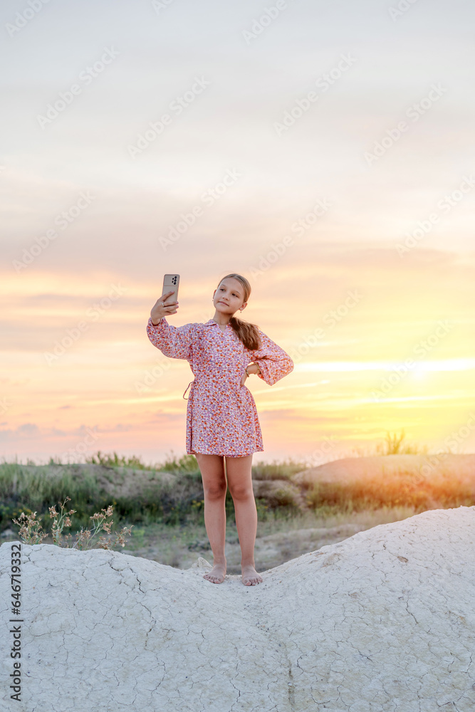 A teenage girl photographs the sunset on mobile phone, recreation and entertainment for children in nature.