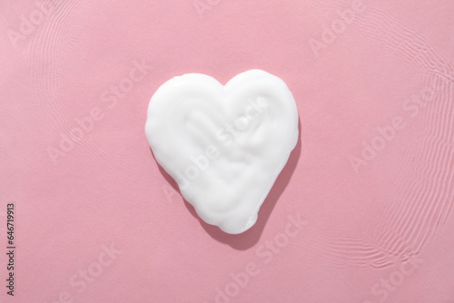 Hand cream in the shape of a heart, close-up, on a pink background.
