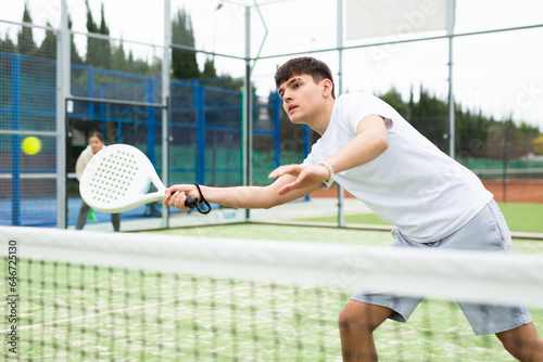 Young European male player serving ball during training padel in court outdoors in spring © JackF