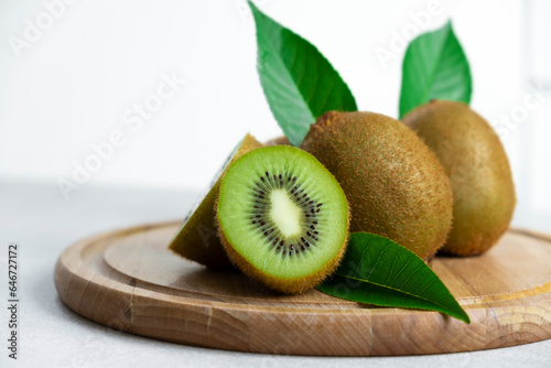 Ripe kiwi fruits in sunlight. Heap of whole kiwi fruits with green leaves and fresh cut kiwi on wooden cutting board. Healthy organic fruits full of vitamins and antioxidants.