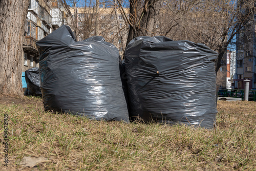 Two black bags with garbage, old fallen leaves, branches on the ground. Spring cleaning. City street cleaning