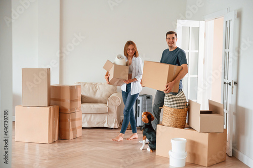 Walking forward with boxes. Young couple with dog are moving to new home photo