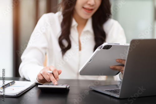 Businesswoman working with tablet and using a calculator to calculate the numbers of static in office. Finance accounting concept.