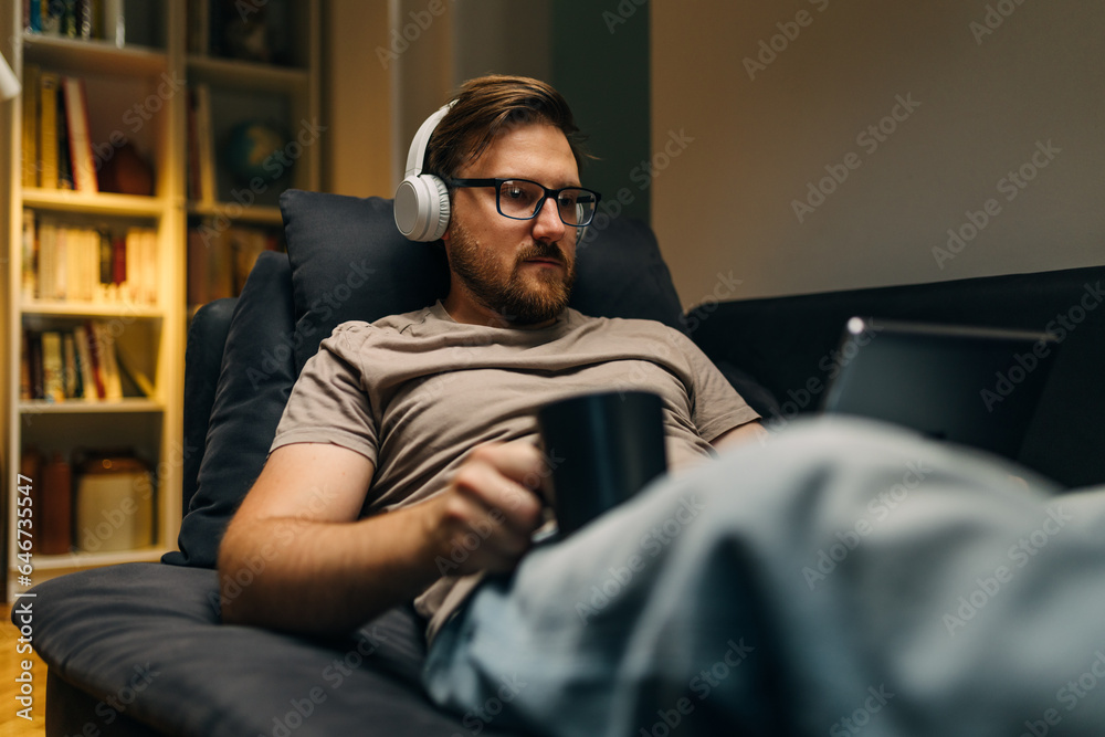 A man is watching a move at home with headphones.