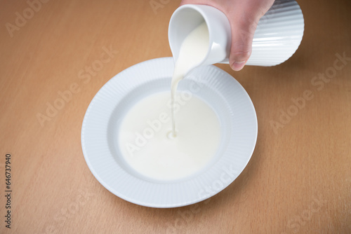 Bowl of milk product being poured from a jug, made in white ceramic.