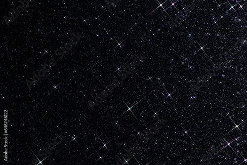 Sparkling texture. Abstract black background with sparkles in the shape of stars. Festive backdrop for your projects. Starry night sky