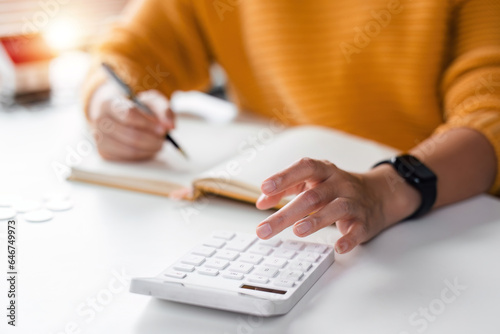 Close up asian women is keeping a record of her income and expenses, she plans her finances by using his monthly savings to buy funds to make it grow faster. Concept of saving money for investment