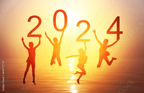 Happy new year card 2024. Silhouette of children girl is jumping on tropical beach with fantastic sunset sky background. Kids holding the number 2024 with sea and sunrise background.