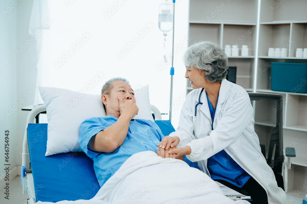 Asian doctor in white suit take notes while discussing and Asian elderly, man patient who lying on bed with receiving saline solution in hospital or clinic. Asian doctor in white suit take notes while discussing and Asian elderly, man patient who lying on bed with receiving saline solution in hospital or clinic.