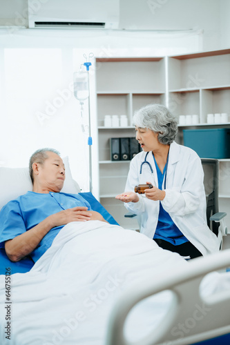 Asian doctor in white suit take notes while discussing and Asian elderly  man patient who lying on bed with receiving saline solution in hospital or clinic.