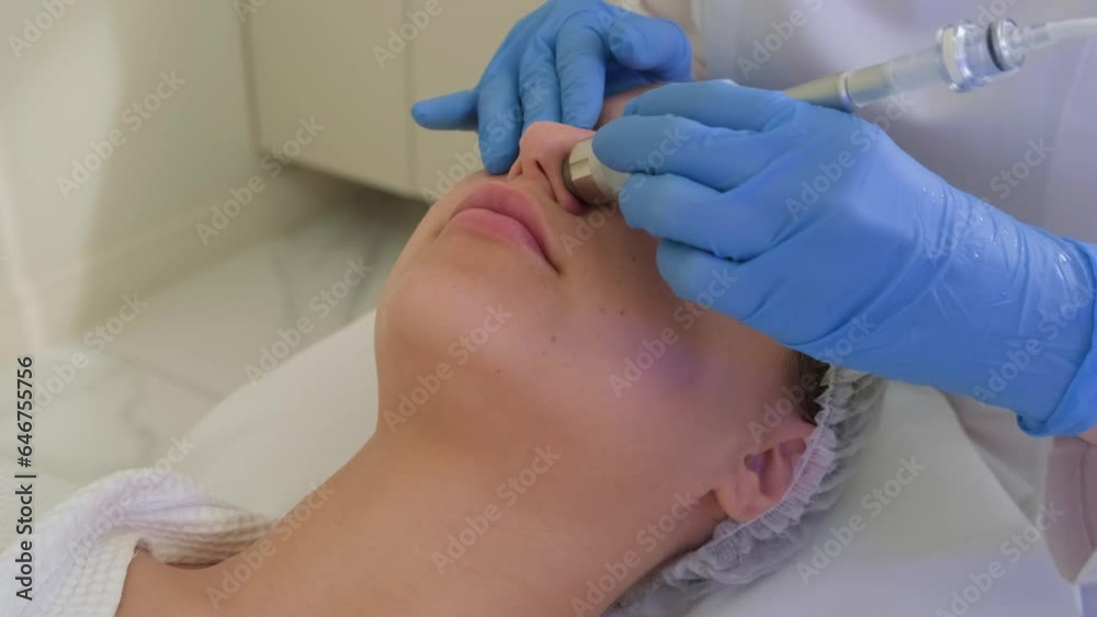 Professional dermatologist in medical gloves doing vacuum peeling procedure for beautiful woman patient in cosmetology clinic. Close-up of hardware facial cleansing. Professional dermatologist in medical gloves doing vacuum peeling procedure for beautiful woman patient in cosmetology clinic. Close-up of hardware facial cleansing.