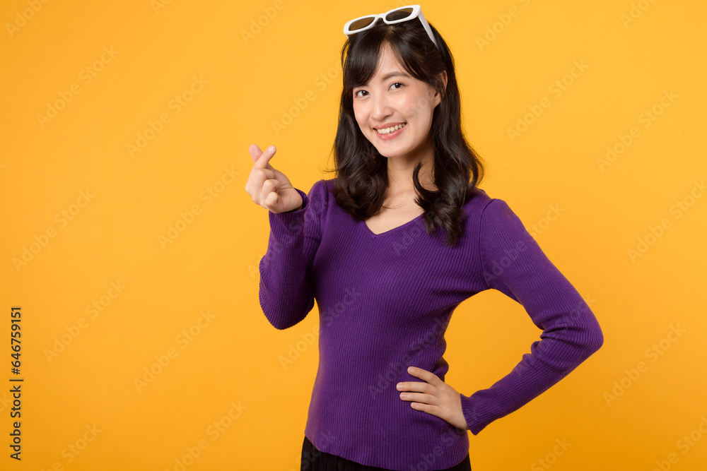 Young Asian 30s woman wearing purple shirt with happy smile showing mini heart sign isolated on yellow background, Speading love and happiness concept Young Asian 30s woman wearing purple shirt with happy smile showing mini heart sign isolated on yellow background, Speading love and happiness concept
