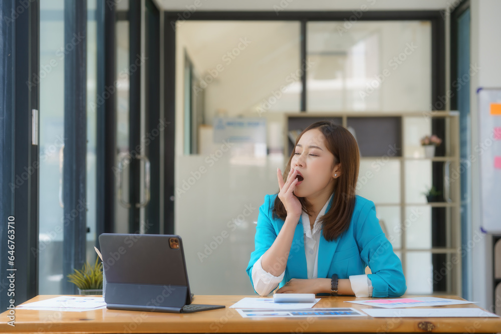 Asian businesswoman yawning while working with a laptop computer.