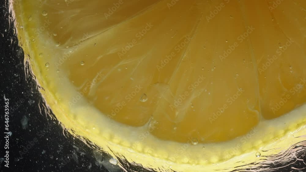 A lemon slice glides on glass with honey and dissolves it with its juice, macro shot against a black background.