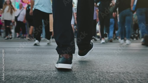 Rear back view following male feet steps crossing busy street. Man wearing casual dark trousers leather sneakers goes on pedestrian crossing in big city. Low angle people crowd legs walking sidewalk