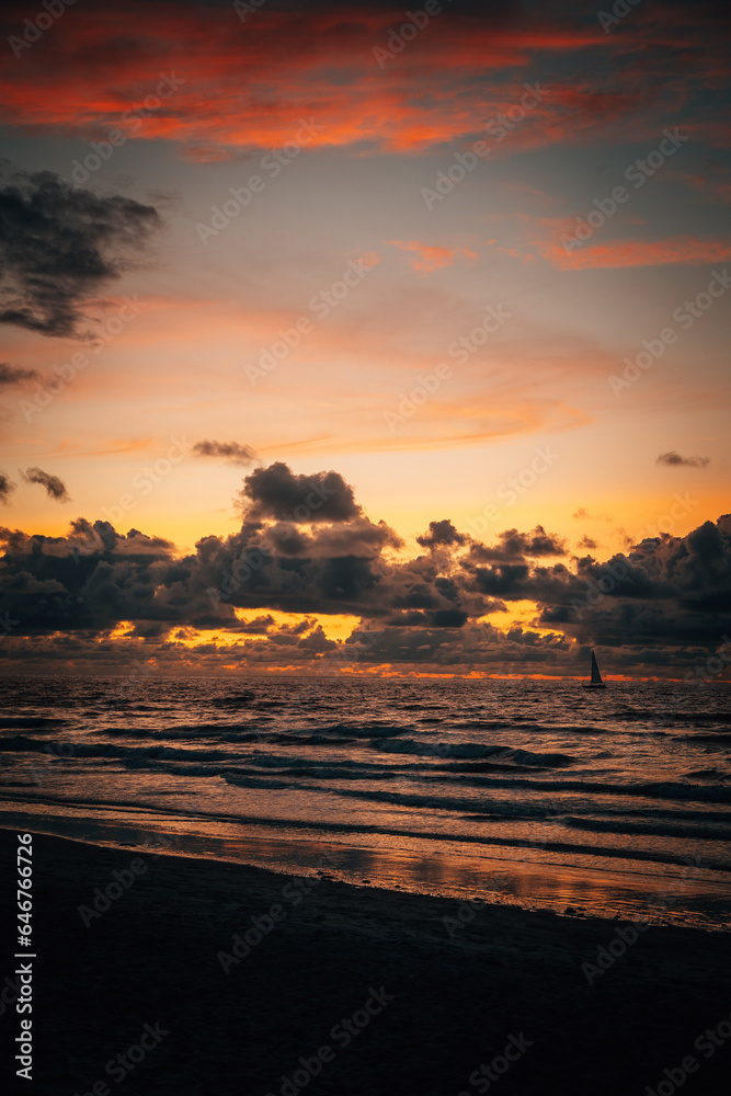 Small sail boat on the sea with a dramatic cloudy yellow and orange sunset over the water