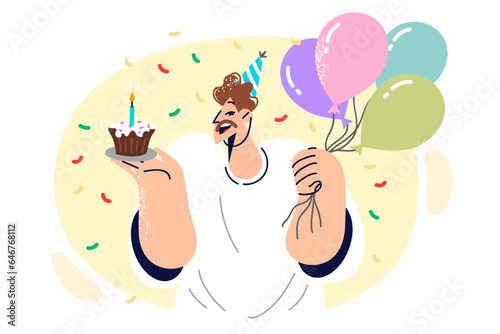 Man celebrating birthday holds piece of cake and balloons, rejoicing at onset of anniversary