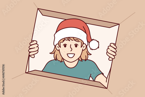 Little girl unpacks christmas gift and with smile looks into cardboard box presented by santa claus. Happy preteen child eagerly opens christmas present from parents or grandparents