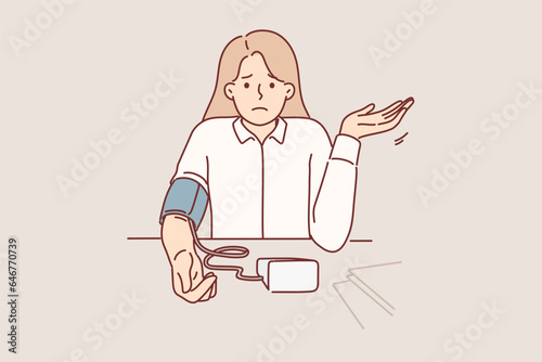 Woman measures blood pressure with electronic tonometer, sits at office desk and feels worse