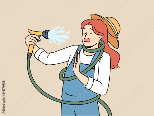 Clumsy woman with garden hose accidentally sprays herself with water while watering backyard lawn during drought. Girl got tangled in garden hose due to failure or lack knowledge of safety precautions