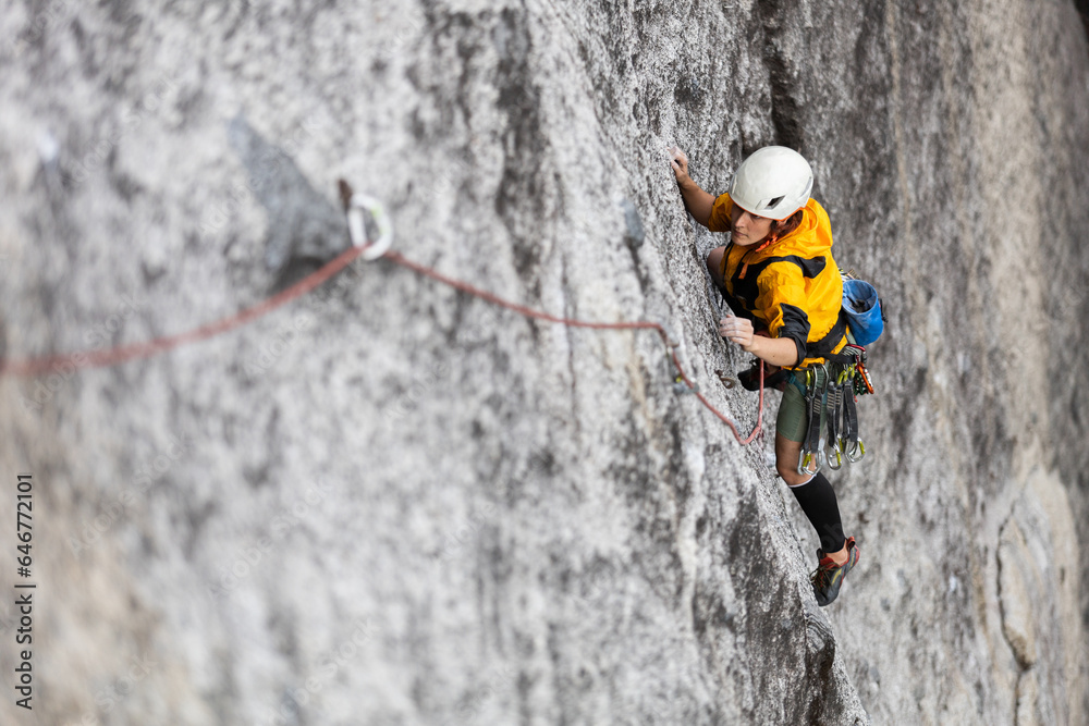 Fototapeta premium Person climbing in high mountains with yellow jacket rope and helmet in nature, confidence and risk, safety