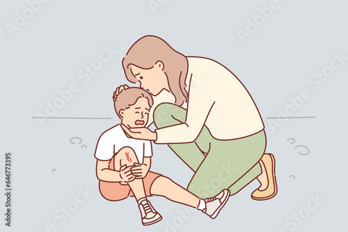 Caring mother consoles crying son who injured knee in fall, kissing child and provides support