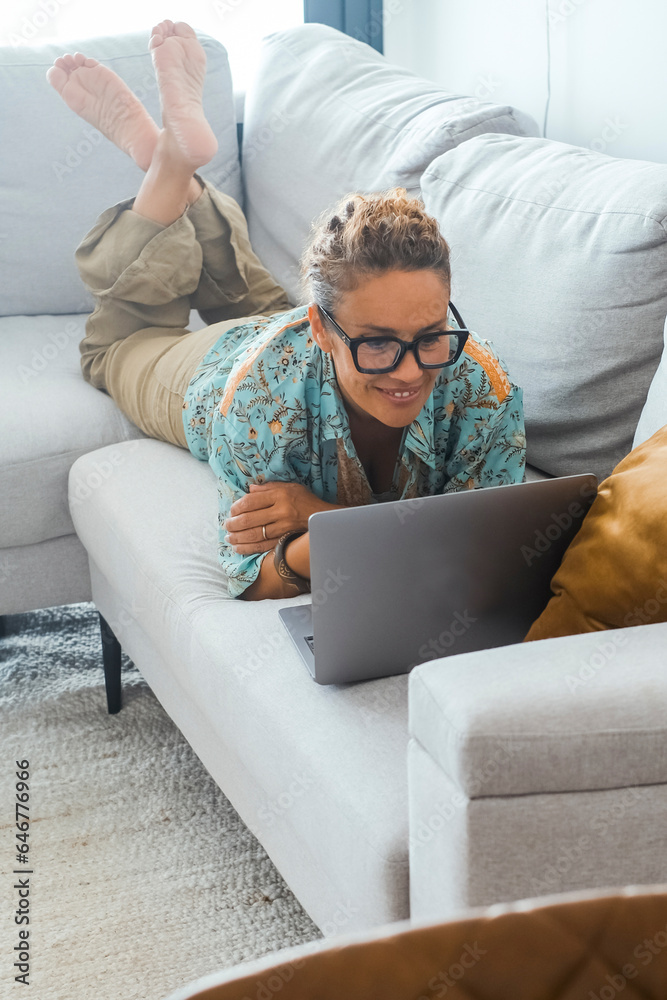 Smart working and surfing the net. One woman at home laying on sofa having relax and indoor technology leisure activity with wireless connection. Modern people lifestyle using laptop on the couch