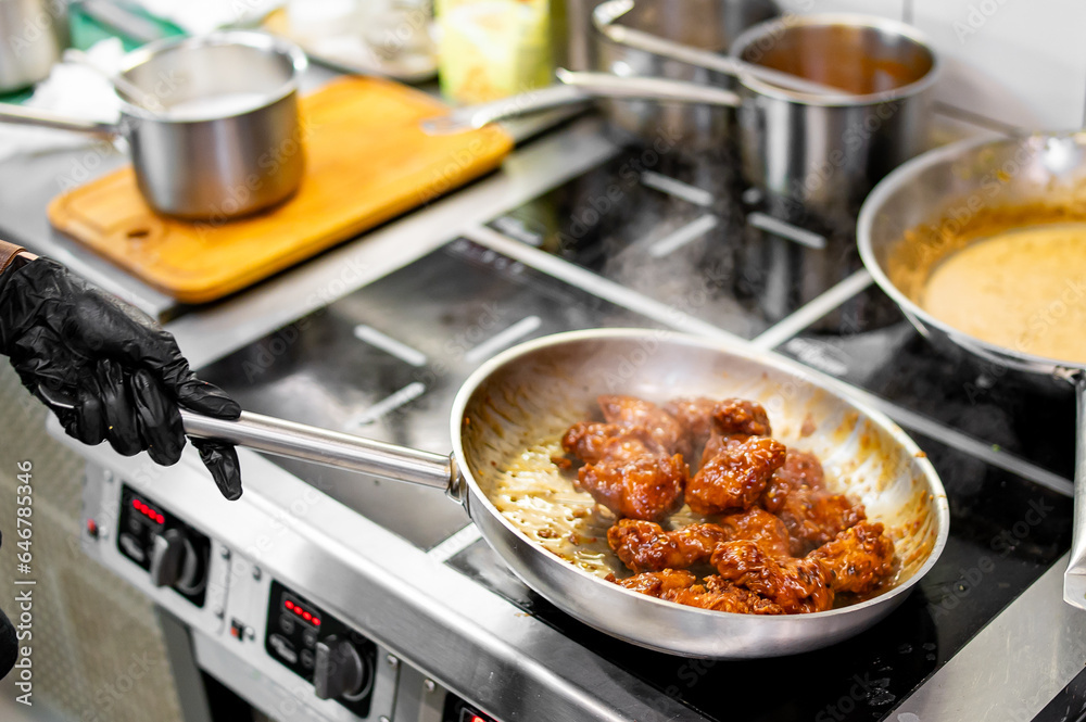 woman chef cooking chicken wings in a sauce on pan in the kitchen woman chef cooking chicken wings in a sauce on pan in the kitchen