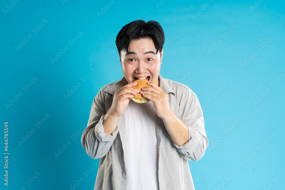 Portrait of asian man eating fast food on blue background Portrait of asian man eating fast food on blue background
