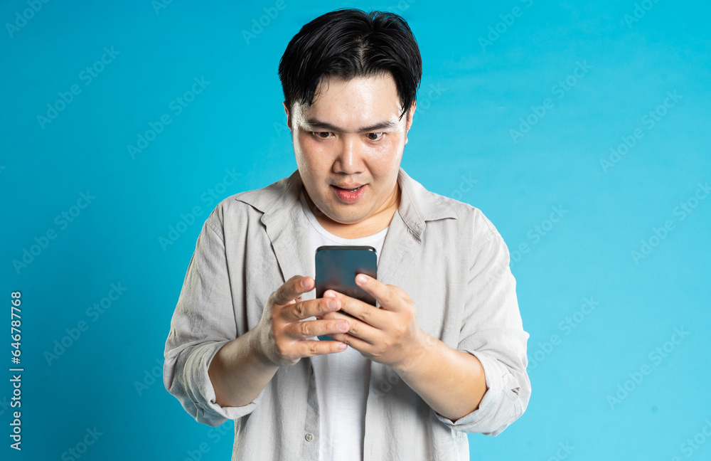 Image of Asian man using phone on blue background Image of Asian man using phone on blue background