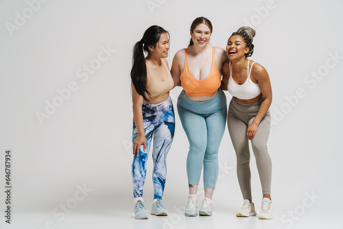 Three cheerful women hugging while standing isolated over white wall