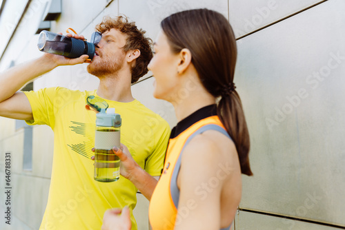 Athletic couple drinking water after workout outdoors