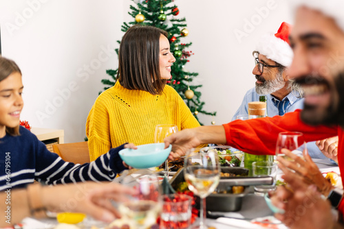 Happy multi generational family gathering at christmas dinner. Diverse people sitting on table celebrating xmas holiday together. Older man talking with her granddaugther. photo