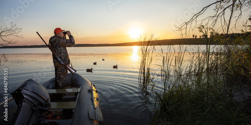hunter looking through binoculars at sunset. waterfowl hunter on boat at lake. banner with place text.