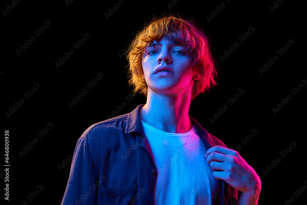 Portrait of young man in casual clothes posing against black studio background in neon lights. Concept of human emotions, facial expression, youth, lifestyle, casual fashion. Ad Portrait of young man in casual clothes posing against black studio background in neon lights. Concept of human emotions, facial expression, youth, lifestyle, casual fashion. Ad