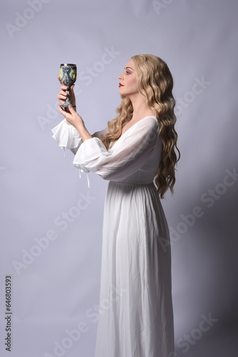 Close up portrait of beautiful blonde model wearing elegant white halloween gown, a historical fantasy character. Holding wine goblet, isolated on audio background.