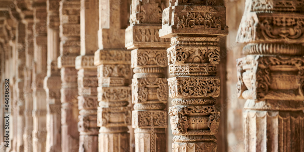 Stone columns with decorative bas relief of Qutb complex in South Delhi, India, close up pillars in ancient ruins of mosque landmark, popular touristic spot in New Delhi, ancient indian architecture