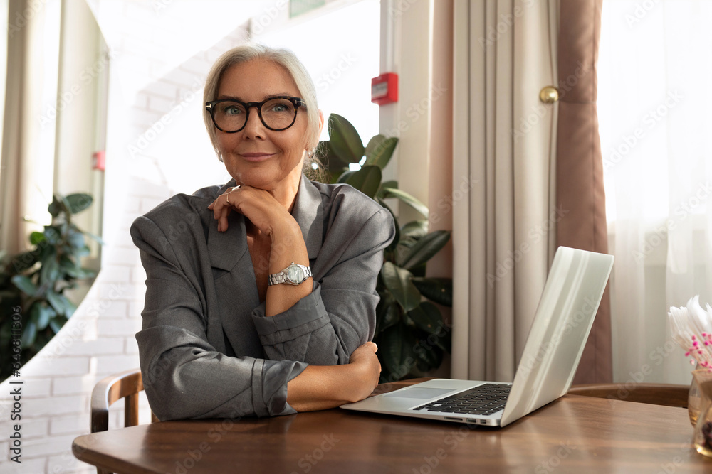 gray-haired mature pretty business woman dressed in a stylish gray jacket sits in a cafe with a laptop gray-haired mature pretty business woman dressed in a stylish gray jacket sits in a cafe with a laptop