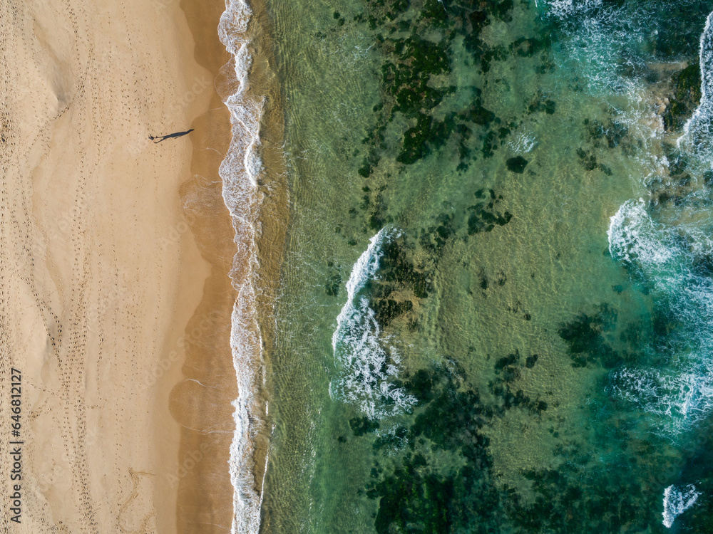 Shadow of person walking along beach with green ocean water and golden sand Shadow of person walking along beach with green ocean water and golden sand