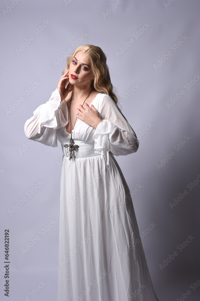 Close up portrait of beautiful blonde model wearing elegant white halloween gown, a historical fantasy character. Holding crucifix cross necklace, isolated on studio background. Close up portrait of beautiful blonde model wearing elegant white halloween gown, a historical fantasy character. Holding crucifix cross necklace, isolated on studio background.