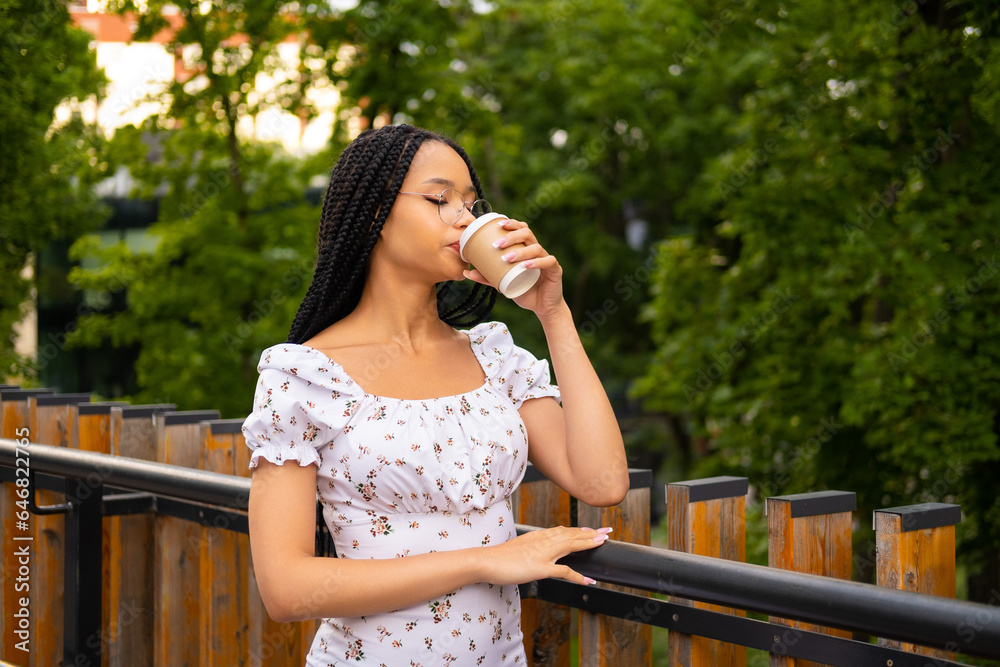Portrait of a young attractive African woman with glasses drinking coffee on the street during the day in the park in summer Portrait of a young attractive African woman with glasses drinking coffee on the street during the day in the park in summer