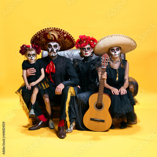 Adorable skeleton posing on yellow background. Happy mexicans family, parents and childrens with creative spooky makeup celebrating Halloween.