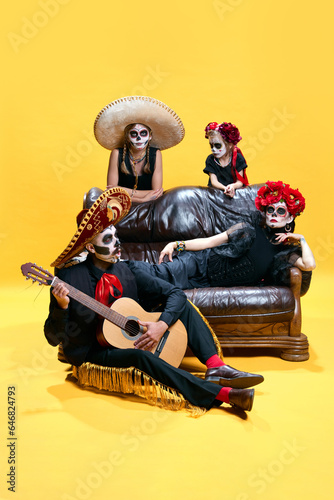 Halloween Family. Father playing on guitar, mother and children in halloween mexico makeup. Relaxing against yellow background