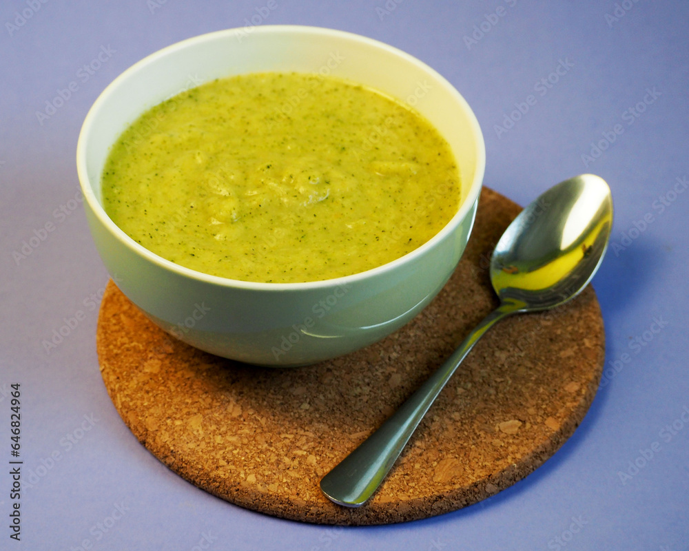 On a purple background there is a plate of broccoli puree soup with a spoon next to it. dinner . gluten-free diet On a purple background there is a plate of broccoli puree soup with a spoon next to it. dinner . gluten-free diet