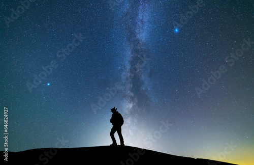 Fantasy landscape, silhouette of a hiker standing on the hill, on the milky way galaxy background.
