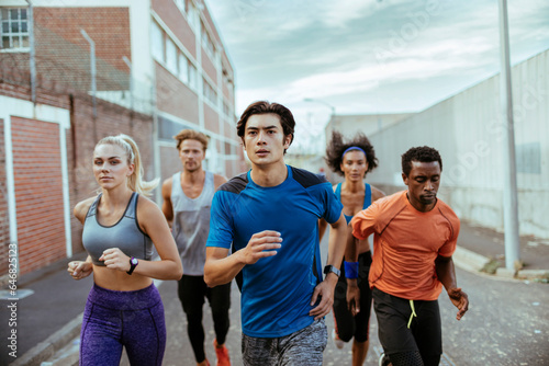 Young and diverse group of friends jogging and running together in the city photo