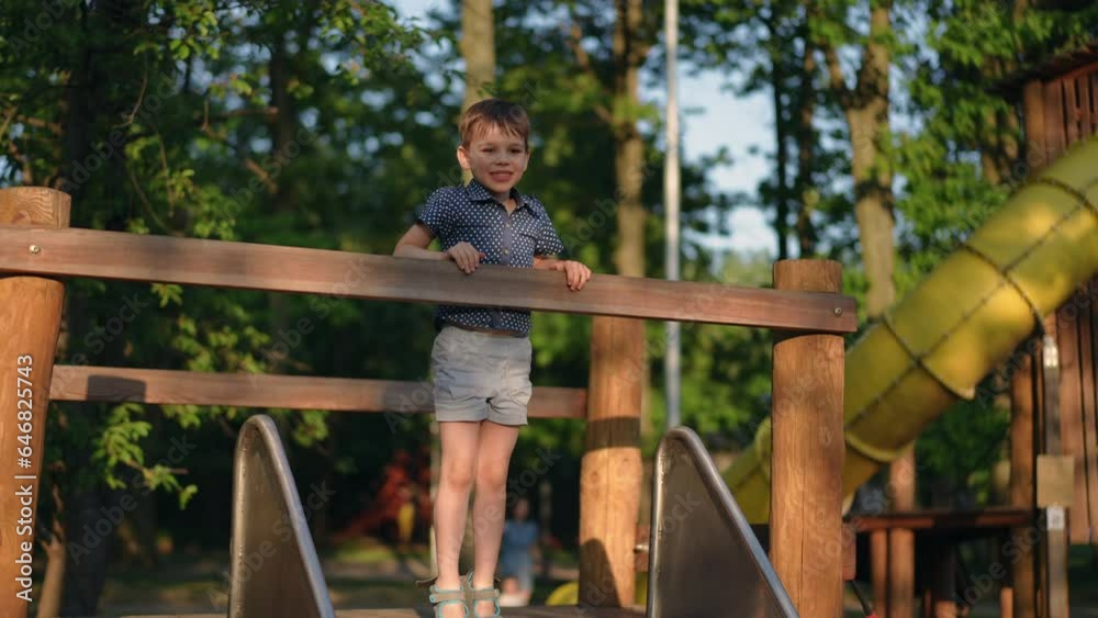 Wide shot hyperactive little boy smiling standing on top holding wooden railing and sliding down slide on playground. Happy excited Caucasian child having fun at sunset in park leaving in slow motion Wide shot hyperactive little boy smiling standing on top holding wooden railing and sliding down slide on playground. Happy excited Caucasian child having fun at sunset in park leaving in slow motion