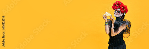 Banner. Young pretty woman in spooky makeup eating delicious hot pizza against bright yellow background. Concept of holiday, party, Halloween