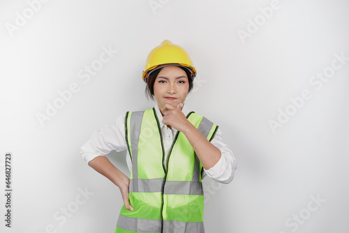 A thoughtful young woman labor worker wearing safety helmet and vest is looking aside to an idea on copy space   isolated by white background. Labor s day concept.